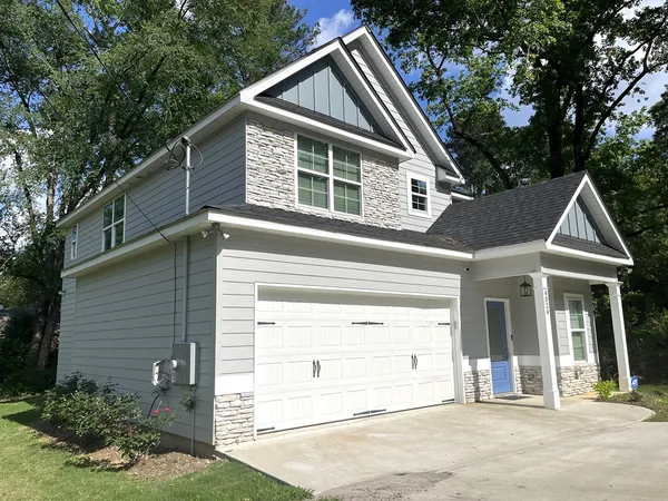 a view of a house with a yard plants and large tree