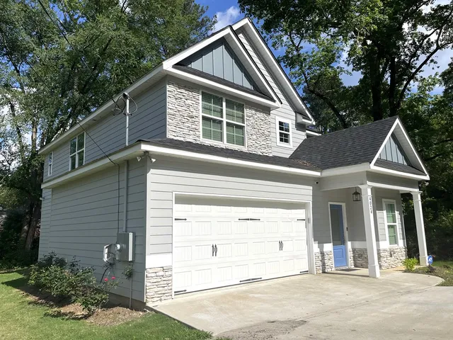 a view of a house with a yard plants and large tree