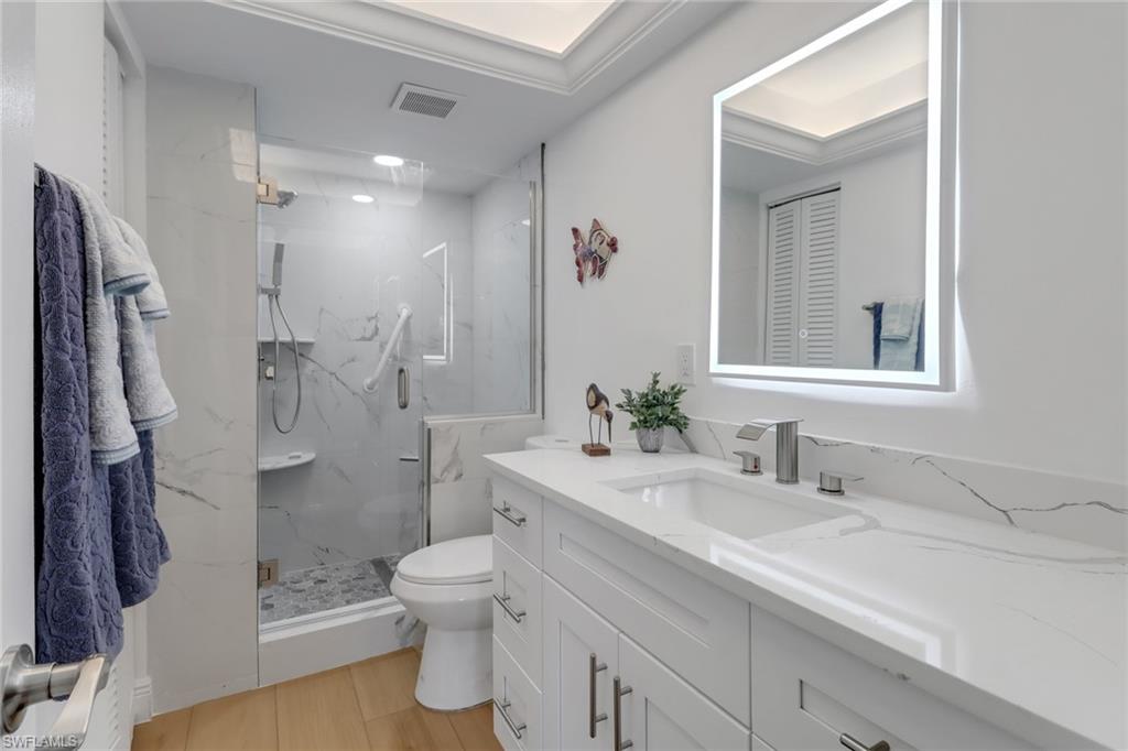 1200 Cherrystone Court, Unit A104 Naples, FL 34102 - Photo 16 of 29 Bathroom with toilet, vanity, a marble finish shower, wood finished floors, and visible vents