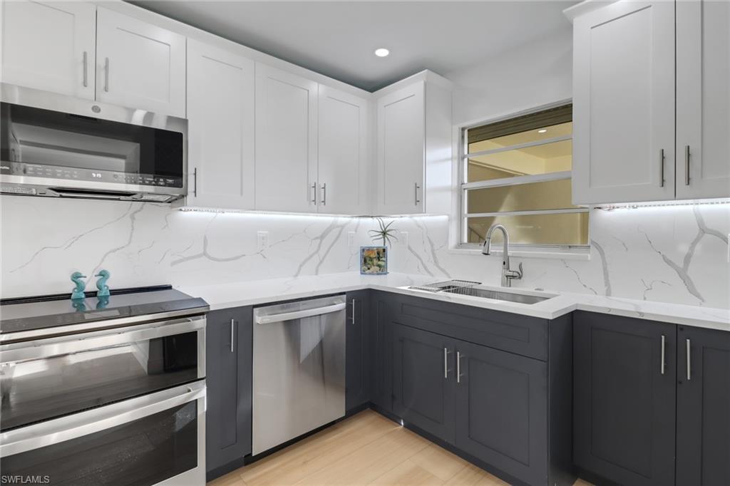 1200 Cherrystone Court, Unit A104 Naples, FL 34102 - Photo 4 of 29 Kitchen with white cabinets, light stone countertops, stainless steel appliances, tasteful backsplash, and a sink