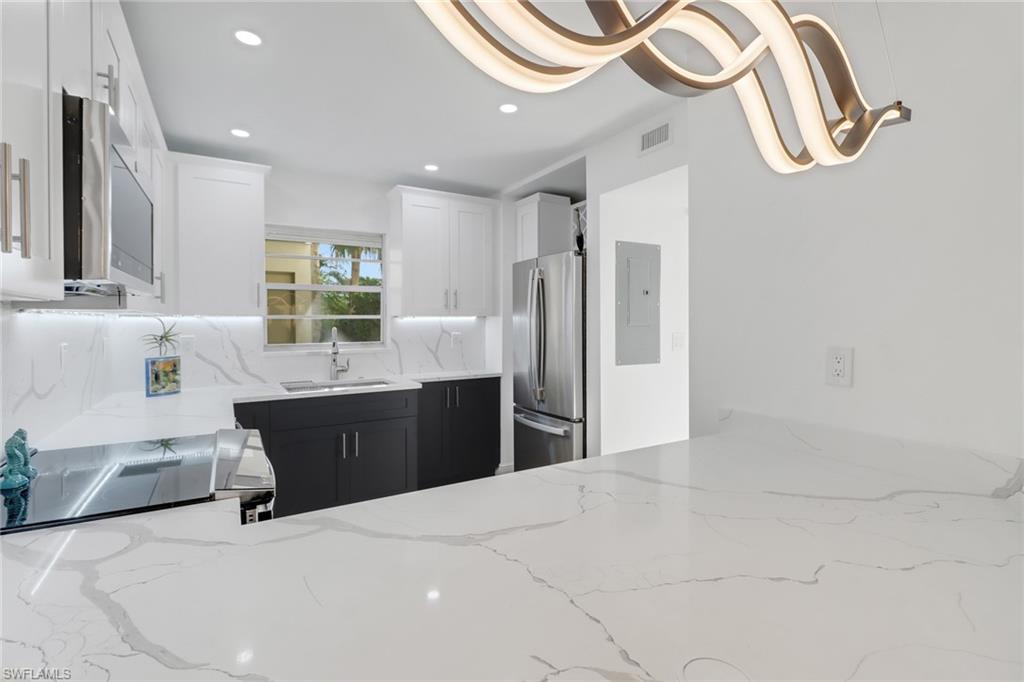 1200 Cherrystone Court, Unit A104 Naples, FL 34102 - Photo 6 of 29 Kitchen featuring visible vents, stainless steel appliances, a sink, dark cabinetry, and light stone counters