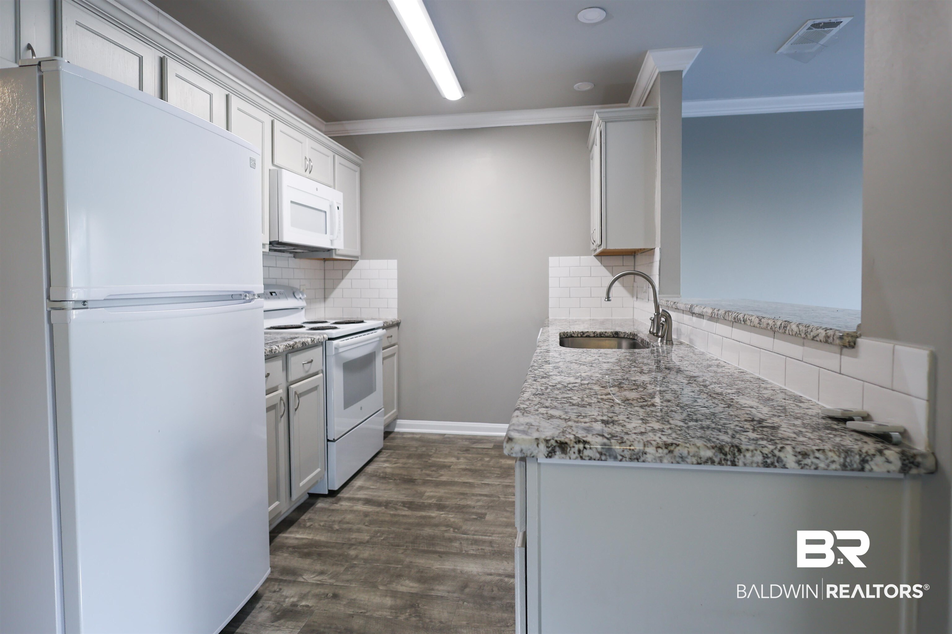 1517 Regency Road, Unit 125 Gulf Shores, AL 36542 - Photo 9 of 26 Kitchen with white appliances, light stone countertops, tasteful backsplash, ornamental molding, and dark wood-type flooring
