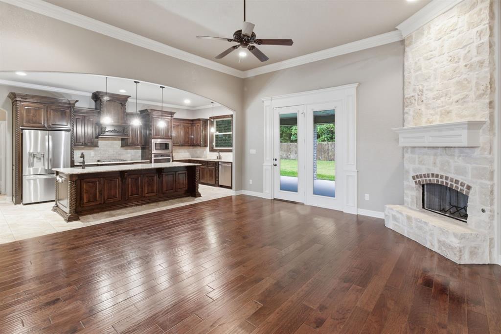 7765 Hickory Spring Lane Tyler, TX 75703 - Photo 15 of 38 Open-concept living area featuring rich wood-finish flooring, a stone fireplace with a white mantel, and glass double doors opening to the exterior