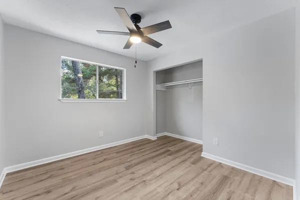 an empty room with wooden floor ceiling fan and windows