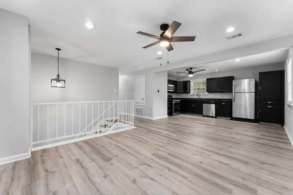 a view of an empty room with wooden floor kitchen view and a window