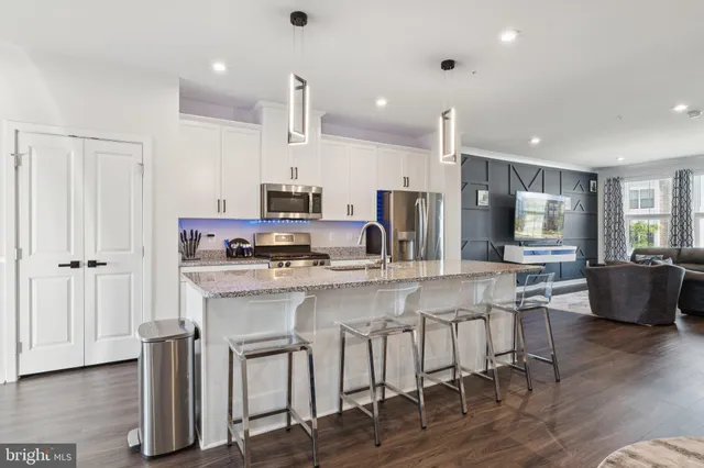 a kitchen with stainless steel appliances granite countertop a refrigerator a stove a sink a dining table and chairs with wooden floor