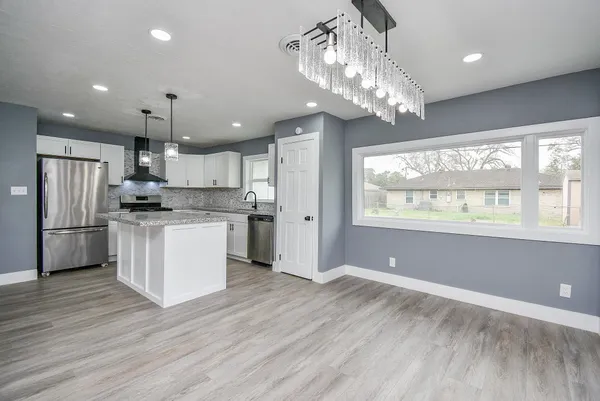 a kitchen with stainless steel appliances granite countertop a refrigerator a sink dishwasher a stove and white cabinets with wooden floor