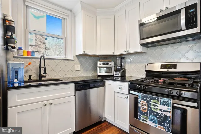 a kitchen with stainless steel appliances granite countertop white cabinets a stove a sink and a microwave