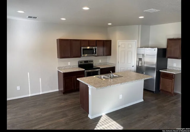 a kitchen with stainless steel appliances a sink a stove a microwave a refrigerator a counter top and cabinets