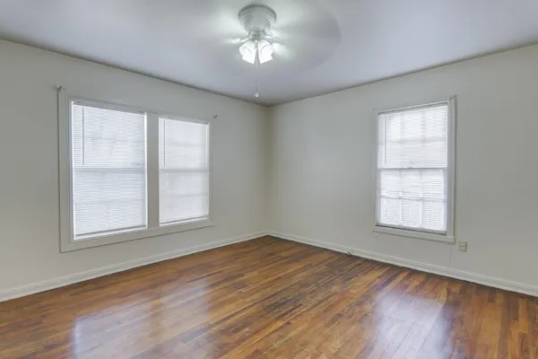 an empty room with wooden floor chandelier fan and windows