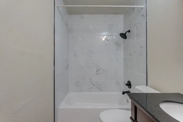 a bathroom with a granite countertop bathtub shower sink vanity and toilet