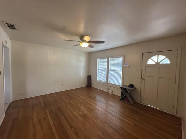 an empty room with wooden floor chandelier fan and windows