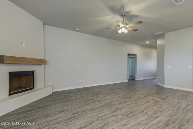 a view of an empty room and kitchen with wooden floor