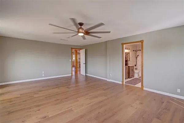 a view of an empty room with wooden floor and a ceiling fan