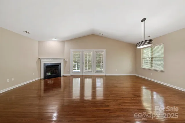a view of an empty room with wooden floor fireplace and a window