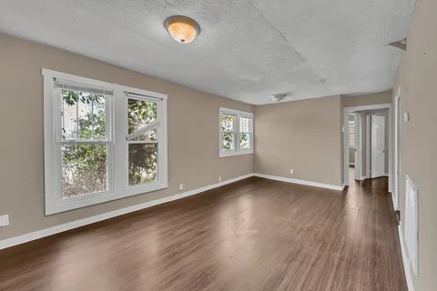 a view of an empty room with wooden floor and a window
