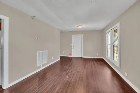 a view of an empty room with wooden floor and a window