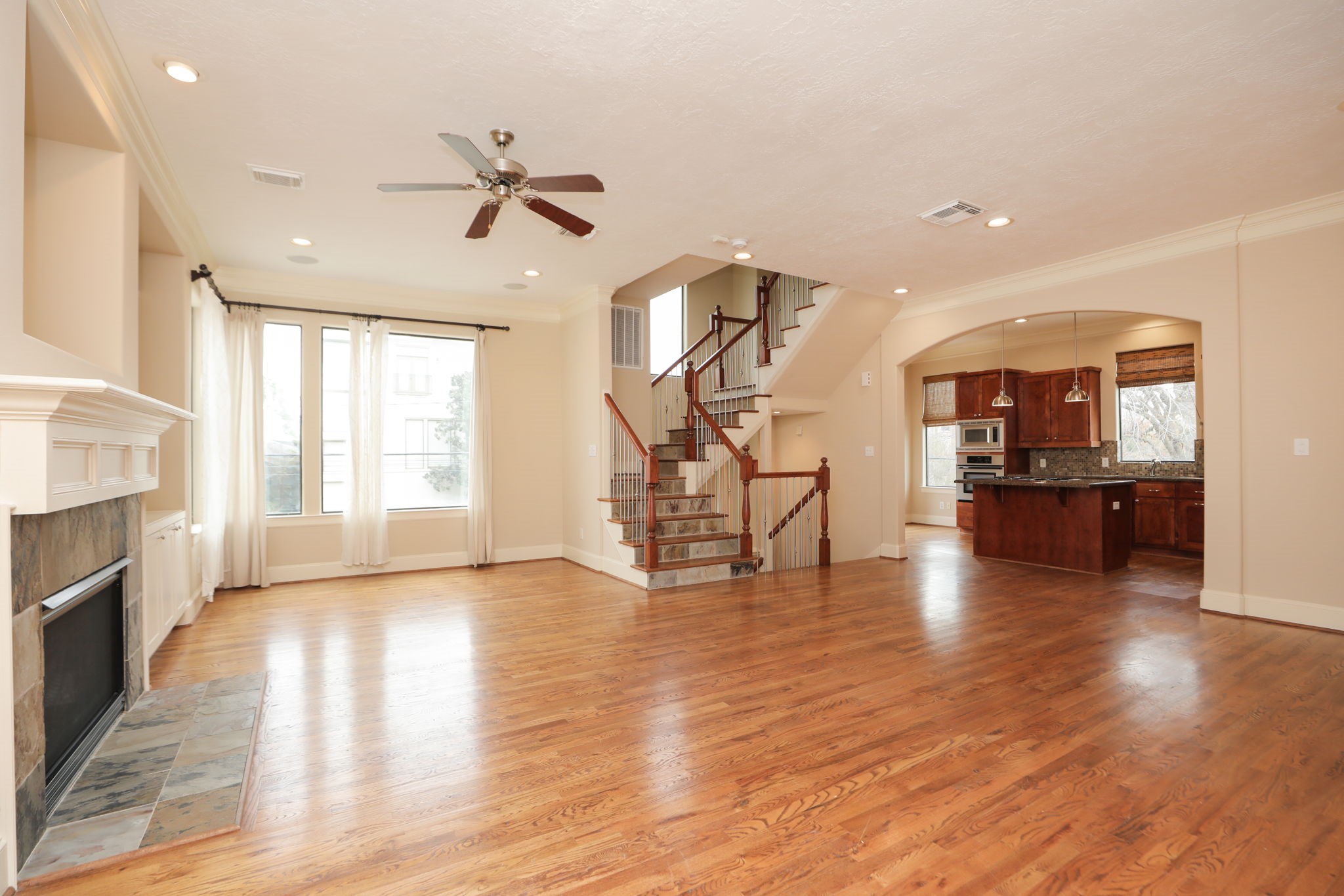 a view of an empty room and kitchen with fireplace wooden floor