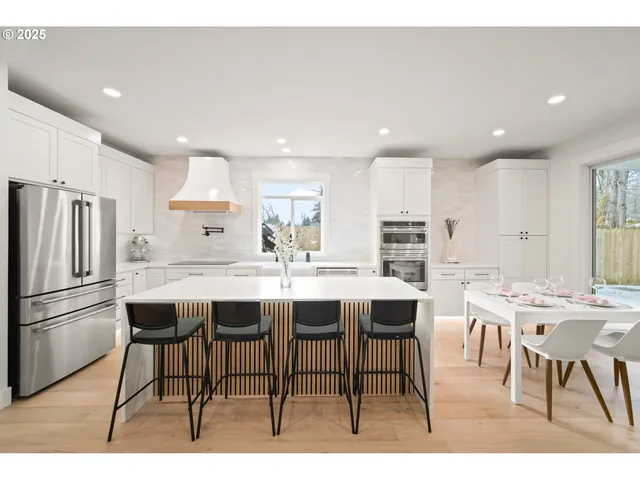 a kitchen with stainless steel appliances kitchen island granite countertop a dining table chairs and a refrigerator