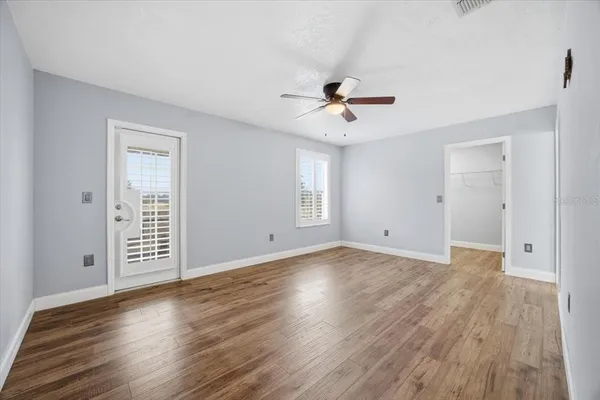 a view of an empty room with wooden floor and a ceiling fan