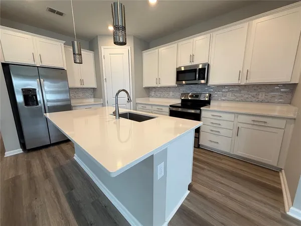 a kitchen with stainless steel appliances granite countertop a sink a stove top oven a refrigerator with white cabinets and wooden floor