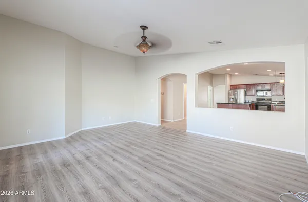 a view of an empty room with wooden floor and a kitchen