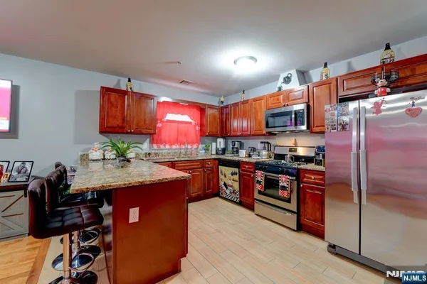 a kitchen with stainless steel appliances granite countertop a stove top oven a sink dishwasher and a refrigerator with wooden cabinets