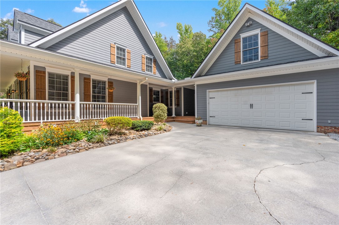A spacious concrete driveway leads toward the charming front porch and attached garage.