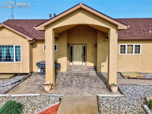 Entrance to property with stucco siding, a shingled roof, and a patio