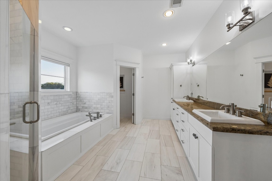3535 Michaux Street Houston, TX 77009 - Photo 28 of 48 This spacious bathroom features a large soaking tub, a separate glass-enclosed shower, dual sinks with a granite countertop, ample cabinet space, and modern fixtures, all accented by bright natural light and sleek tile flooring.