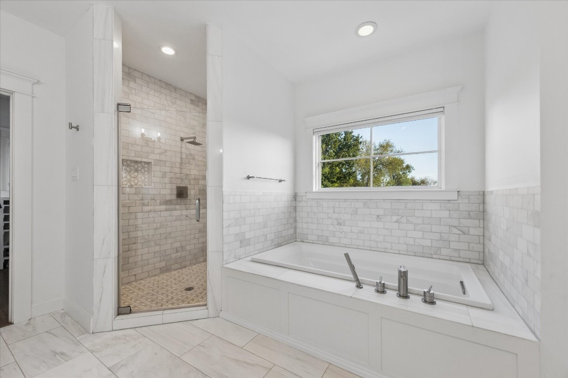 3535 Michaux Street Houston, TX 77009 - Photo 29 of 48 This bathroom features a spacious walk-in shower with glass doors and elegant tile work, alongside a large soaking tub under a bright window, creating a serene and luxurious space.