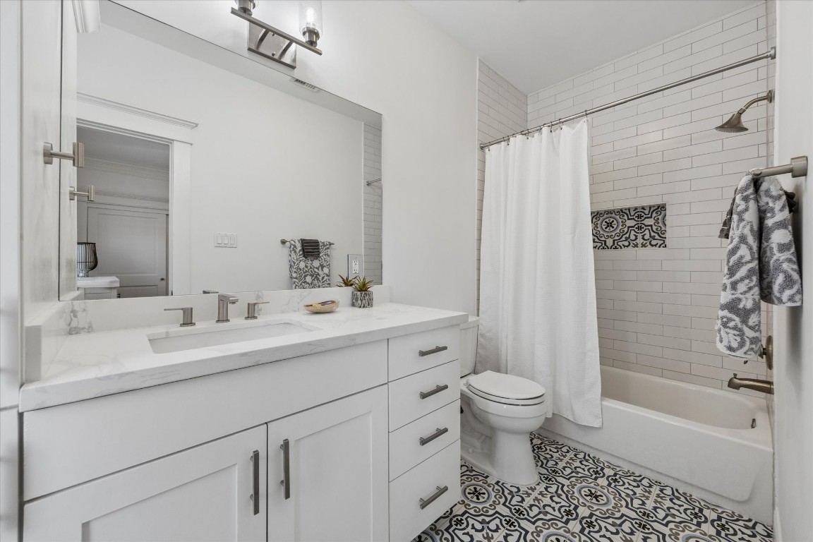 3535 Michaux Street Houston, TX 77009 - Photo 37 of 48 This bathroom features a modern design with a white vanity, marble countertop, and sleek fixtures. The shower has classic subway tiles with a patterned accent, paired with a stylish geometric floor tile. A large mirror and neutral colors enhance the space's brightness and elegance.
