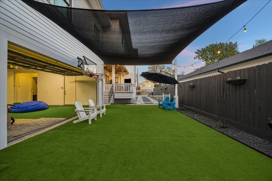 3535 Michaux Street Houston, TX 77009 - Photo 42 of 48 This backyard features a spacious, shaded area with a removable carpet of turf grass, perfect for relaxation or play. It includes ample room for outdoor seating, string lights for ambiance, and a basketball hoop. A suspended sail canopy provides additional shade, and the area is bordered by a privacy fence and a deck leading to the house. Notice that the homeowners have extended the turf area into the garage so that the garage space can be alternatively used as a shady spot for exercise and recreation.