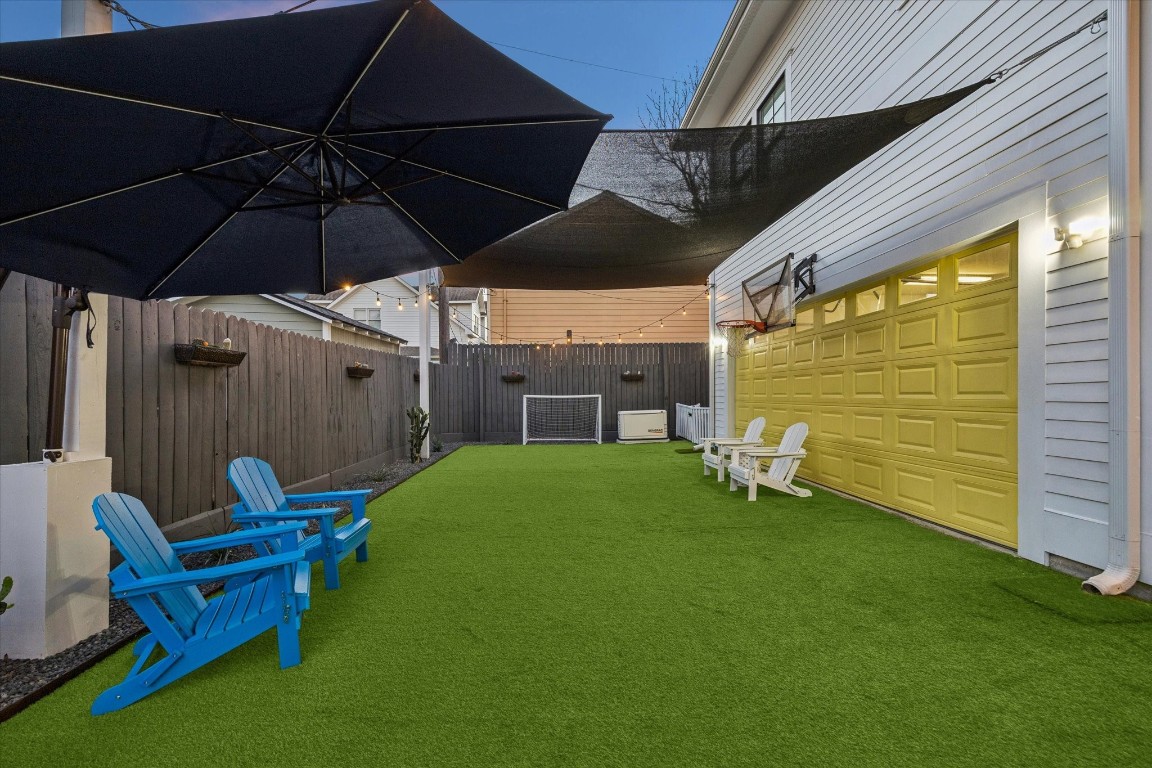3535 Michaux Street Houston, TX 77009 - Photo 44 of 48 Here is another view of the charming backyard with artificial grass, featuring a shaded sitting area with a basketball hoop above a vibrant yellow garage door. Perfect for relaxation and recreation.