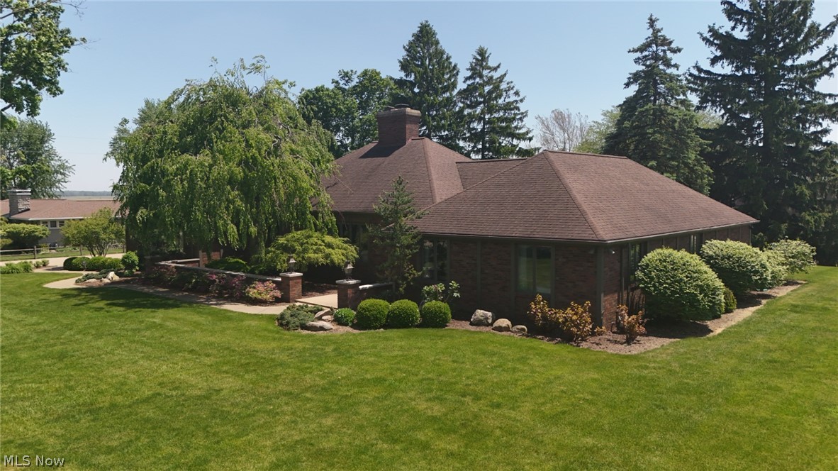 Brick exterior residence with a brown shingle roof, established landscaping, and a manicured lawn