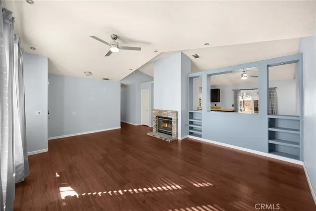 a view of an empty room with wooden floor and a kitchen