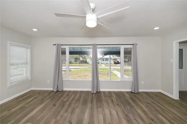 a view of an empty room with wooden floor and a ceiling fan