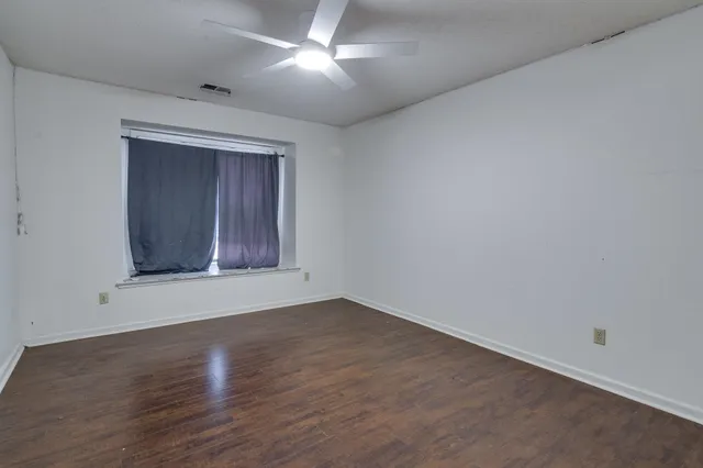 an empty room with wooden floor chandelier fan and windows