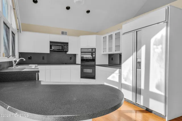 a view of an empty room with wooden floor and a kitchen
