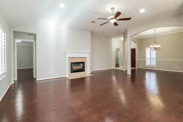 an empty room with wooden floor a ceiling fan a fireplace and windows