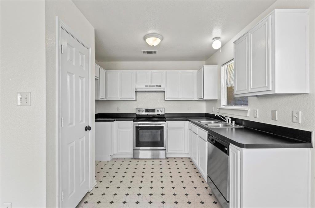 5169 East Rim Road Dallas, TX 75211 - Photo 4 of 19 White kitchen featuring a stainless steel range and dishwasher, dark countertops, white cabinetry, and patterned flooring
