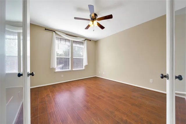 an empty room with wooden floor fan and windows