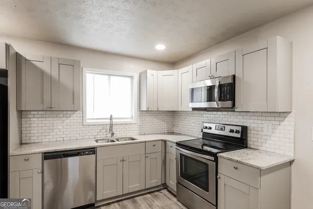 a kitchen with stainless steel appliances granite countertop white cabinets a sink a stove a microwave and a refrigerator