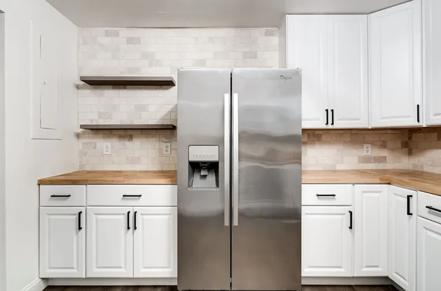 a kitchen with stainless steel appliances granite countertop a refrigerator a sink and white cabinets