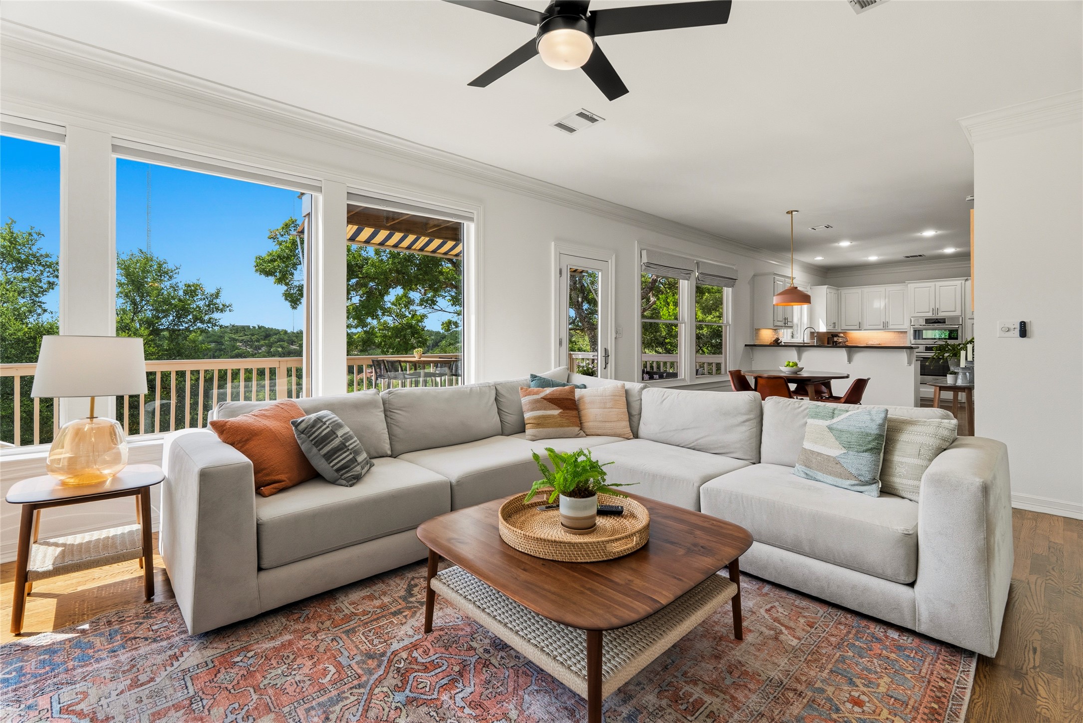 3107 Lookout Lane Austin, TX 78746 - Photo 13 of 39 A spacious living room with hardwood floors opens to a kitchen, bathed in natural light from large windows offering expansive outdoor views.