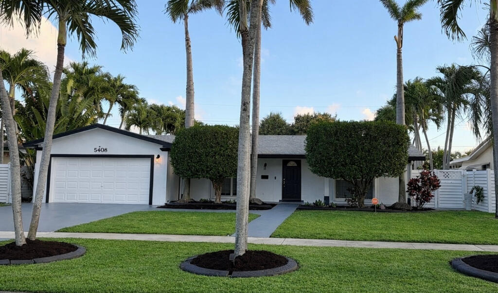 a front view of yellow house with a yard and palm trees