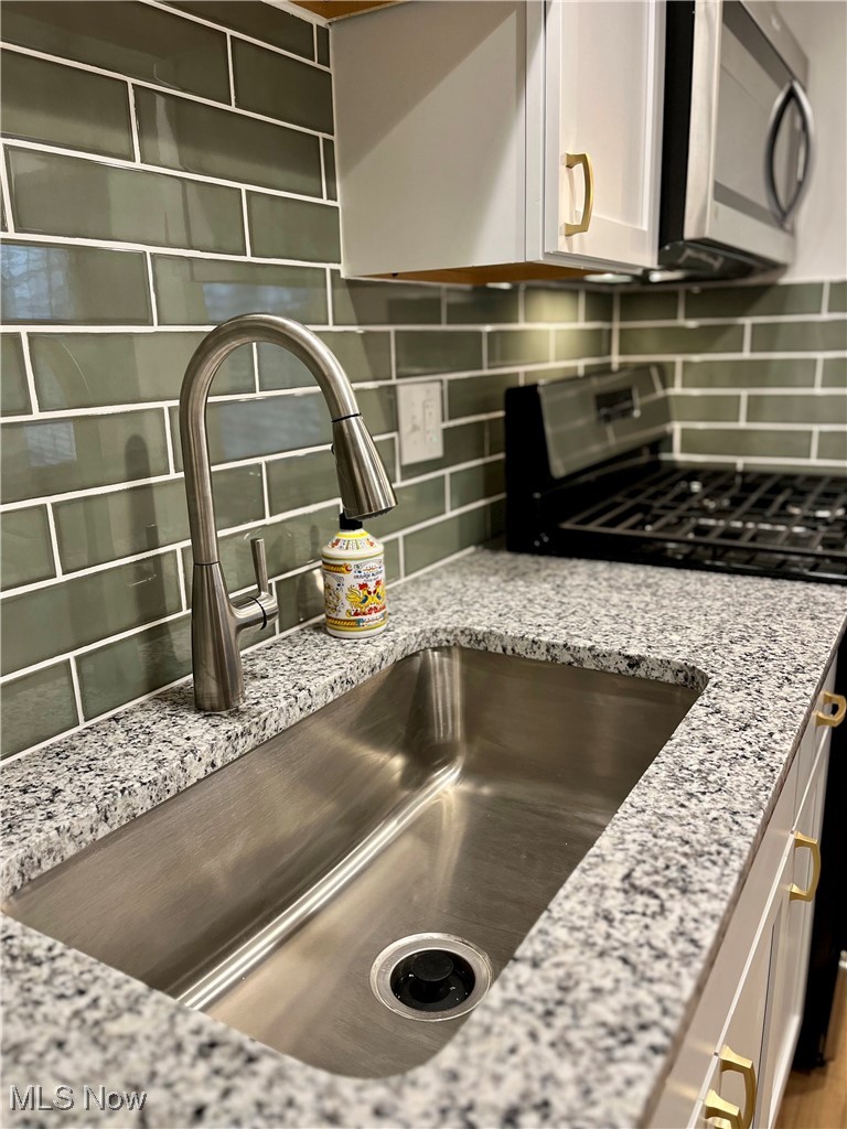 22701 Center Ridge Road, Unit 201 Rocky River, OH 44116 - Photo 12 of 37 Interior details with gas stove, sink, light stone counters, backsplash, and white cabinets