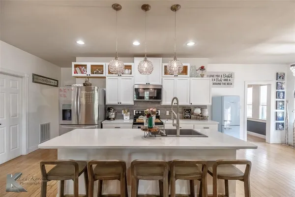 a kitchen with stainless steel appliances granite countertop a dining table chairs and refrigerator