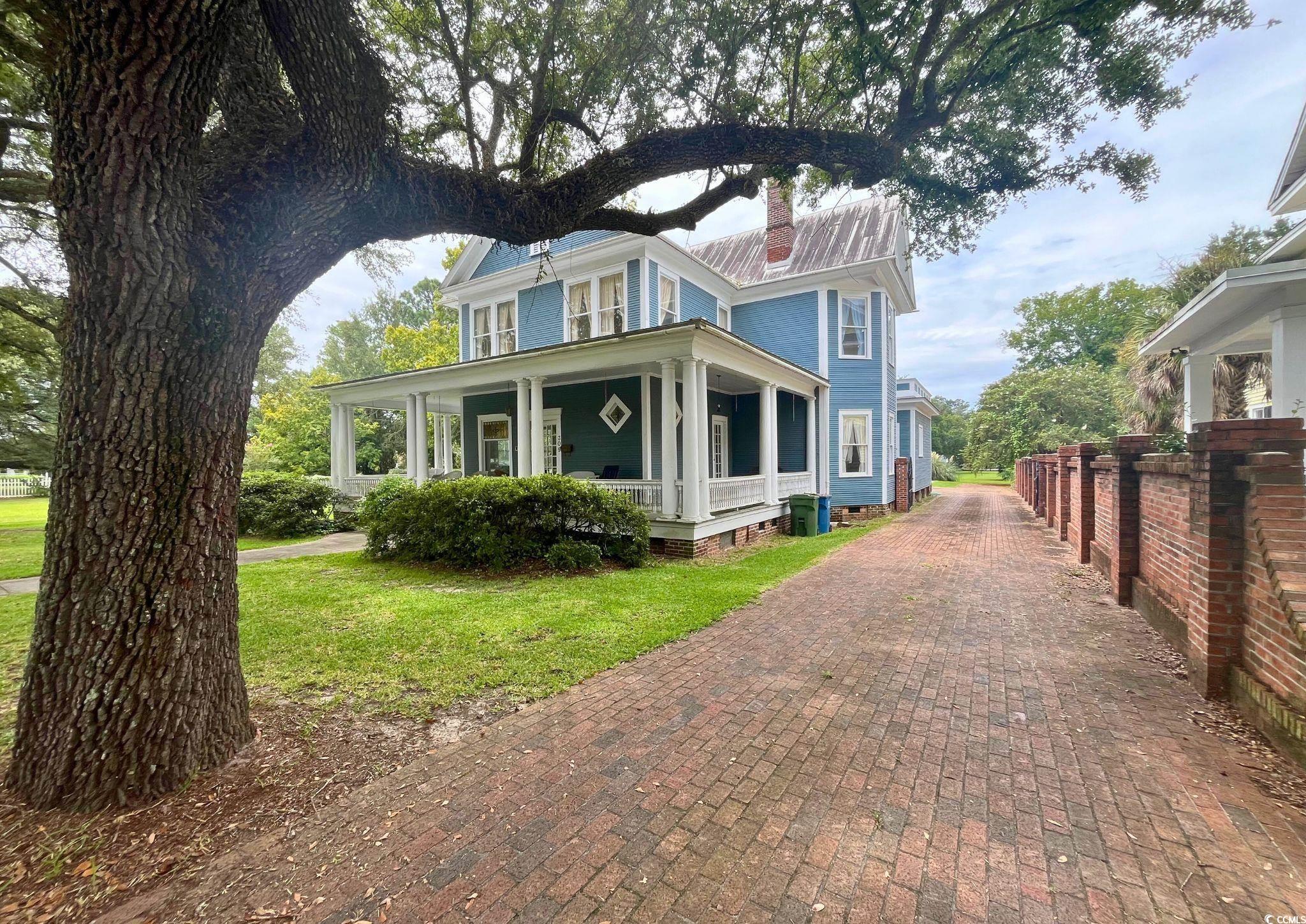View of front facade featuring covered porch, a chimney, a front lawn, and a metal roof