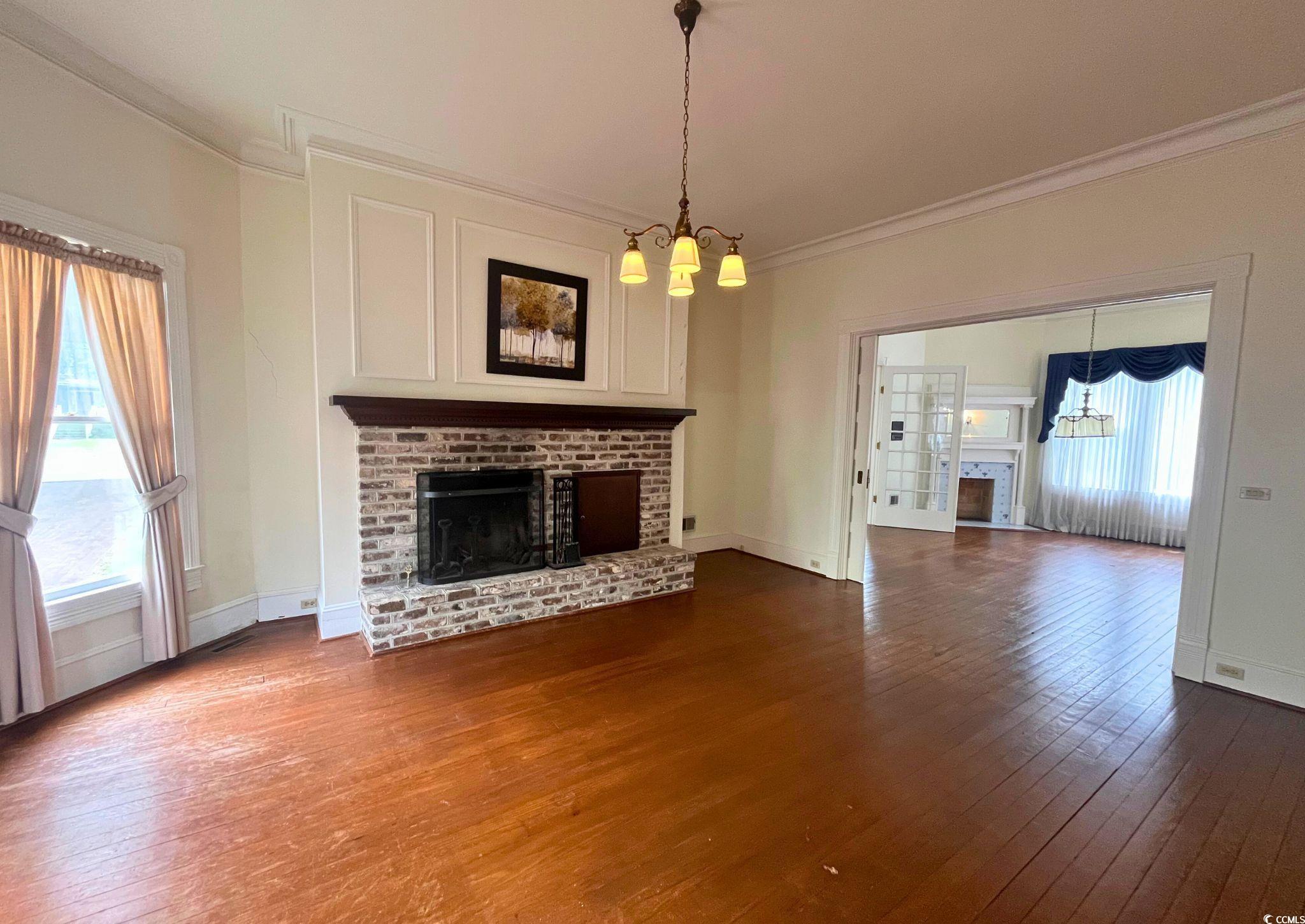 309 North Academy Street Kingstree, SC 29556 - Photo 12 of 38 Unfurnished living room with a brick fireplace, a chandelier, dark wood-style flooring, and crown molding
